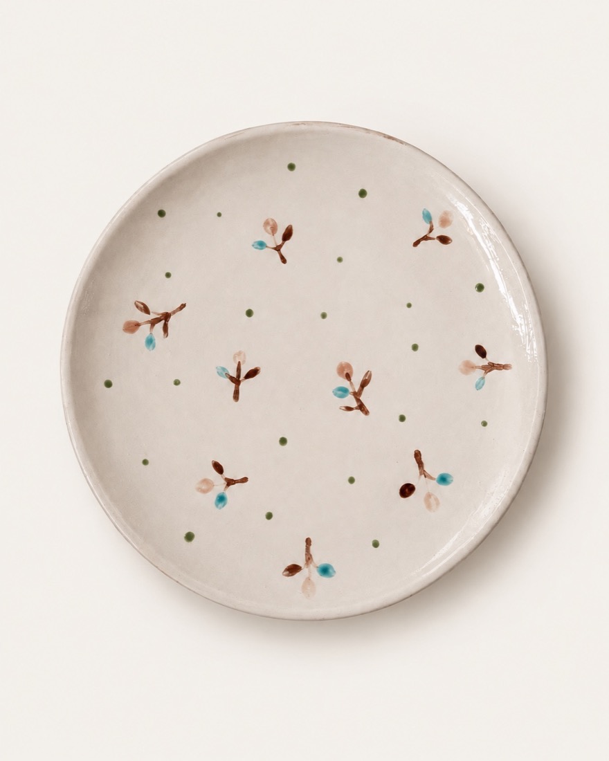 Plato blanco con pequeñas ramitas pintadas en marrón, turquesa y rosa, y puntos verdes